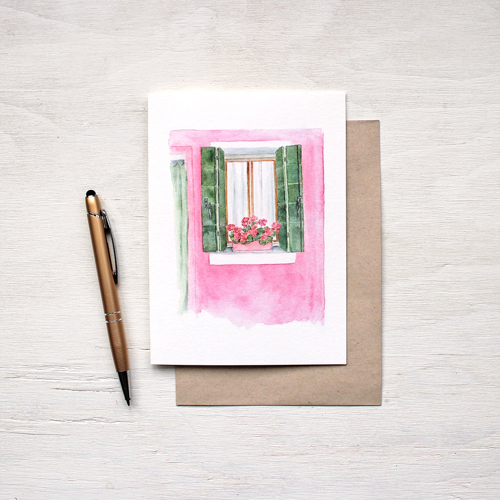 Note card featuring a watercolor painting of a pink house with green shutters and matching geraniums on the windowsill. A scene from Burano, Italy. Artist Kathleen Maunder