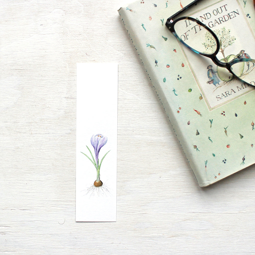 A paper bookmark featuring a watercolour painting of a striped purple crocus bulb. Artist Kathleen Maunder.