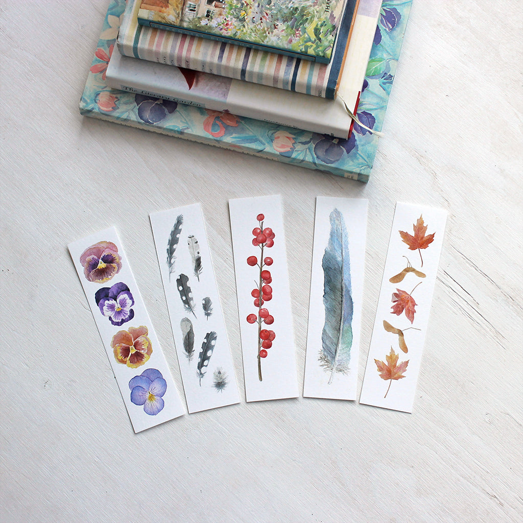 Set of five watercolor bookmarks by Kathleen Maunder. Set includes pansies, woodpecker feathers, winterberries, blue feather and maple leaves.