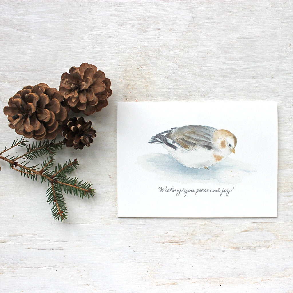 A lovely bird holiday card featuring a delicate watercolor painting of a snow bunting and the hand lettered greeting: 'Wishing you peace and joy'.