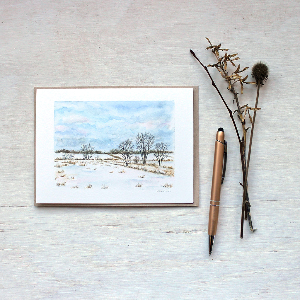 A blank note card featuring a watercolor painting of a snowy rural landscape. Artist Kathleen Maunder.