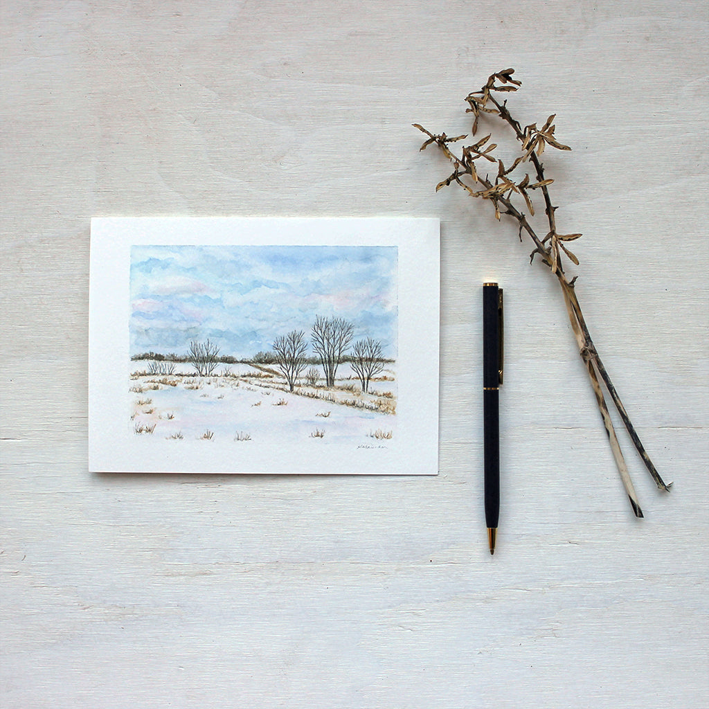 A blank note card featuring a watercolour painting of a snowy rural landscape. Artist Kathleen Maunder.