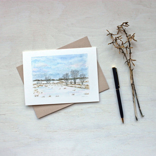 A blank note card featuring a landscape painting of snowy rural fields and a beautiful cloudy sky. Watercolor artist Kathleen Maunder.