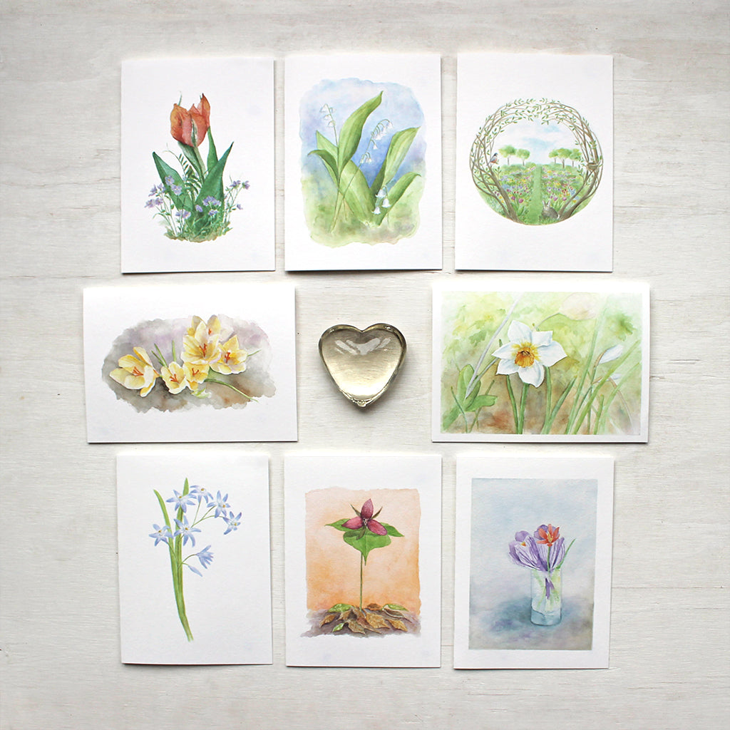 Set of eight spring floral note cards featuring the watercolor artwork of Kathleen Maunder. Images include a tulip and violets, lily of the valley, a secret garden, yellow crocuses, a white daffodil, chionodoxa, a red trillium and a tiny spring bouquet.