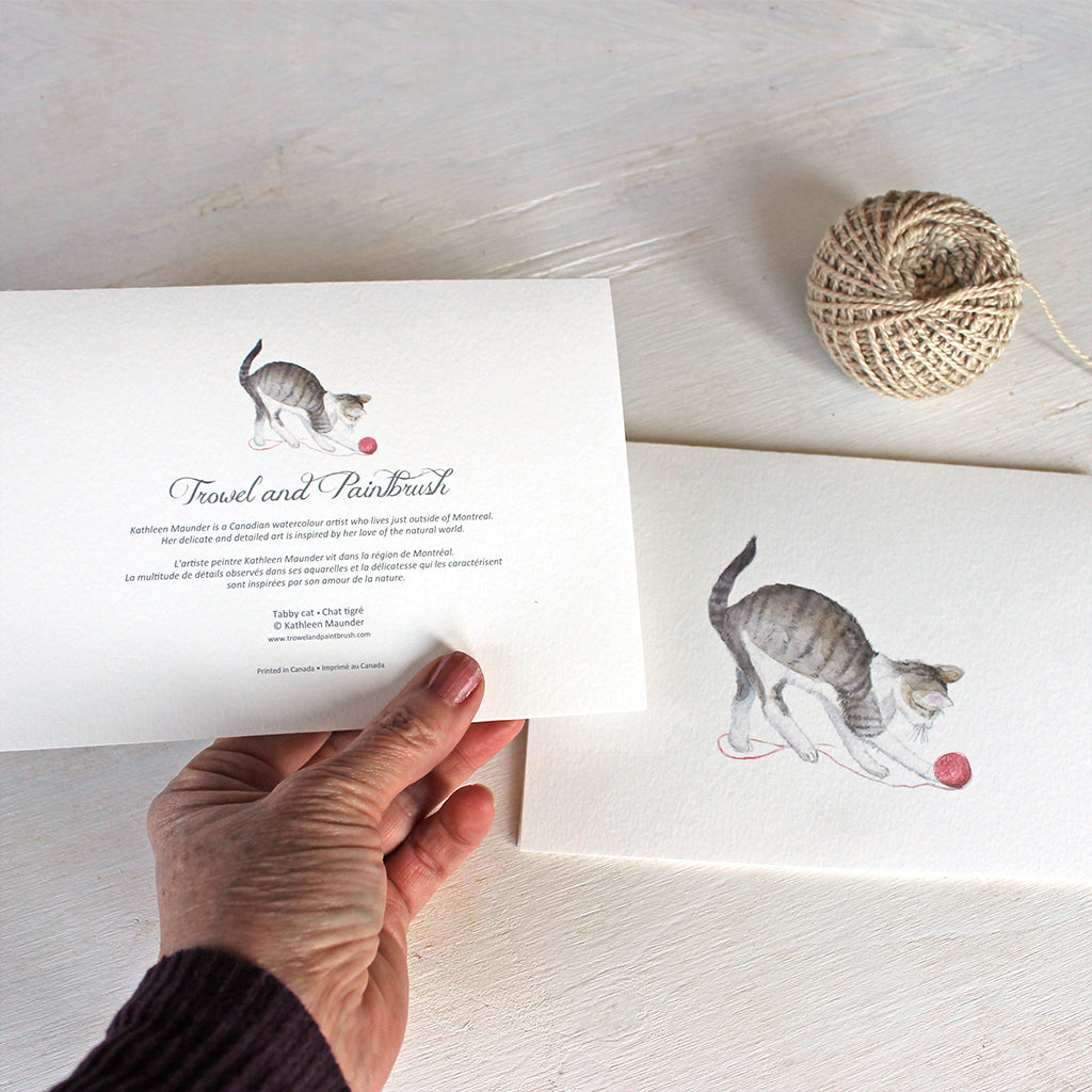 Front and back of a note card featuring a watercolor painting of a tabby kitten playing with a red ball of yarn. Artist Kathleen Maunder.