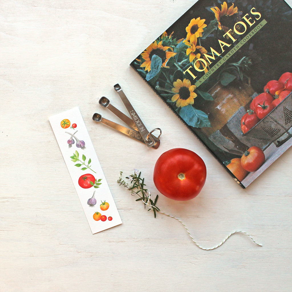 A bookmark featuring watercolor paintings of heirloom garden tomatoes, garlic and basil by artist Kathleen Maunder.