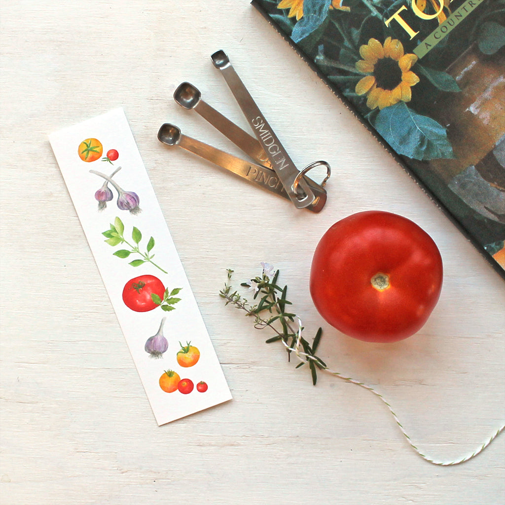 A bookmark featuring watercolor paintings of heirloom garden tomatoes, garlic and basil by artist Kathleen Maunder.