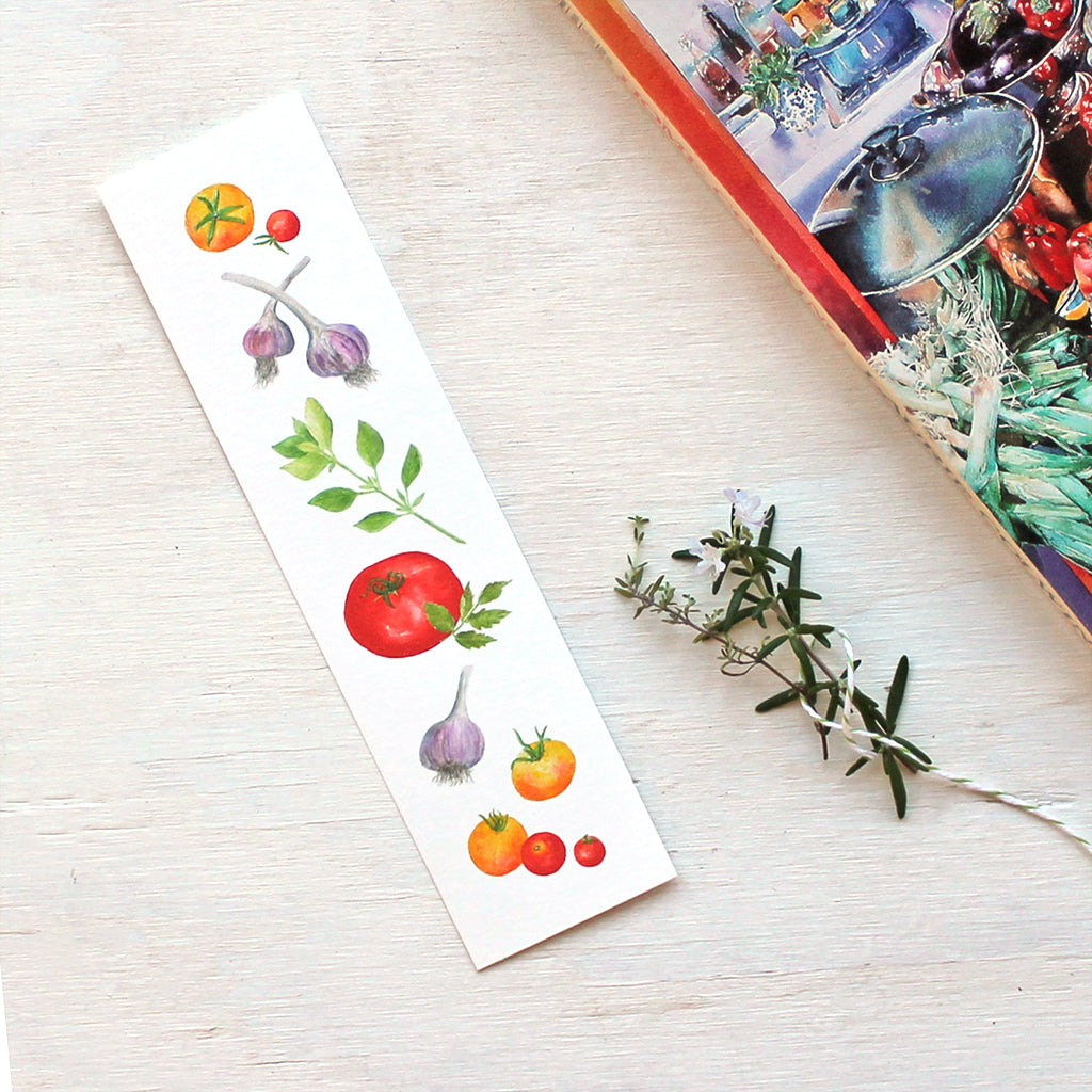 A bookmark featuring paintings of red and yellow heirloom garden tomatoes, purple-striped garlic and basil by watercolour artist Kathleen Maunder.