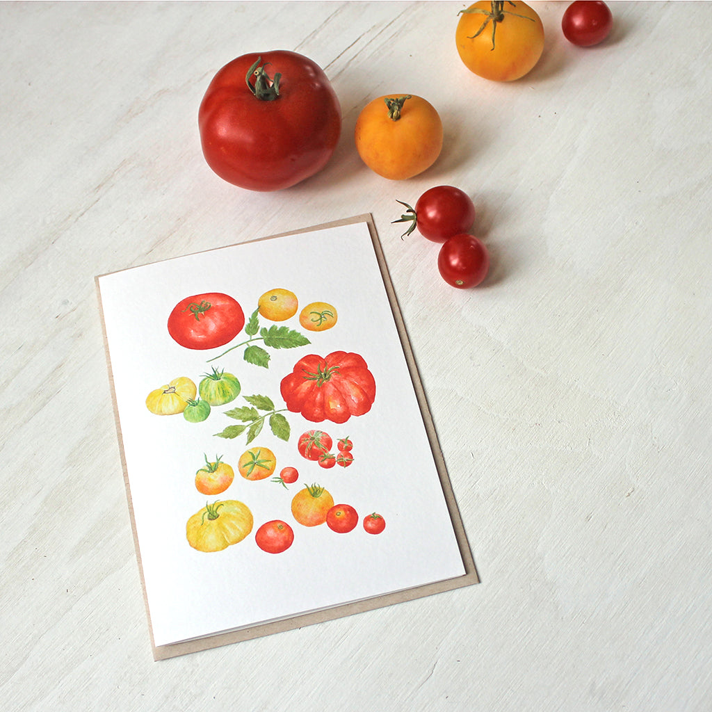 A blank note card featuring a watercolor painting of several types of red, yellow and green heirloom garden tomatoes. Artist Kathleen Maunder.