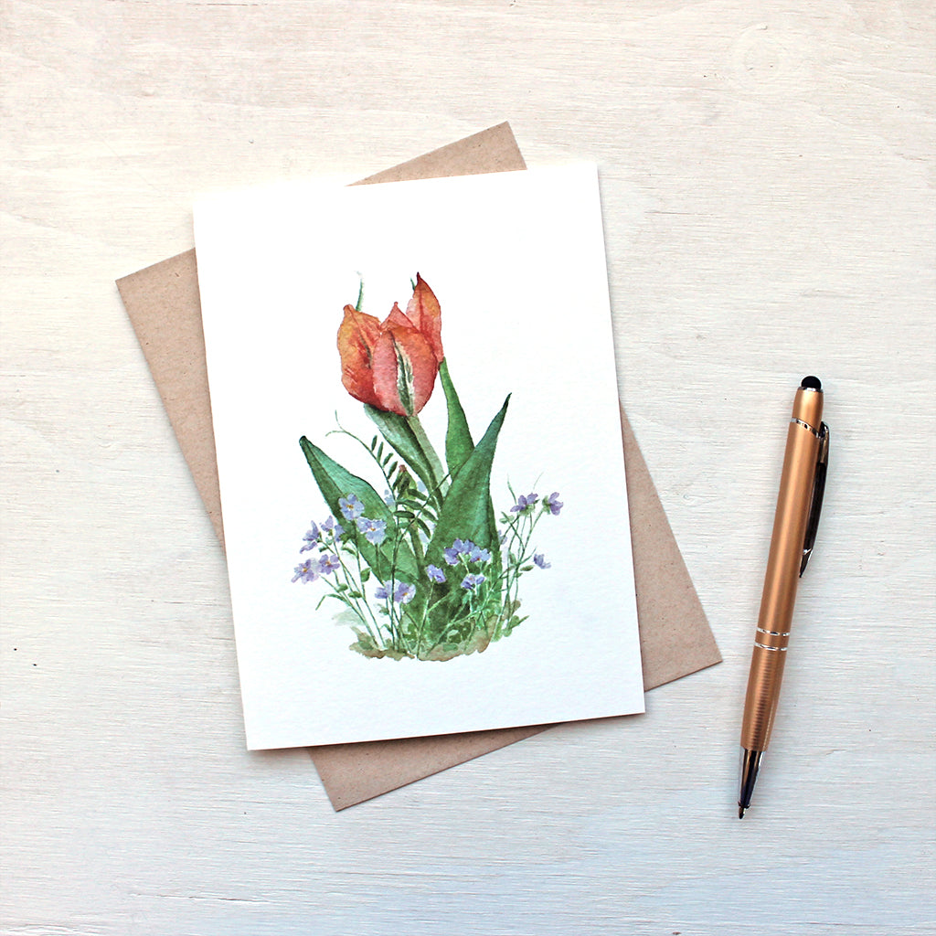 A spring floral card featuring a watercolour painting of an orange and red tulip surrounded by delicate violets. Artist Kathleen Maunder.