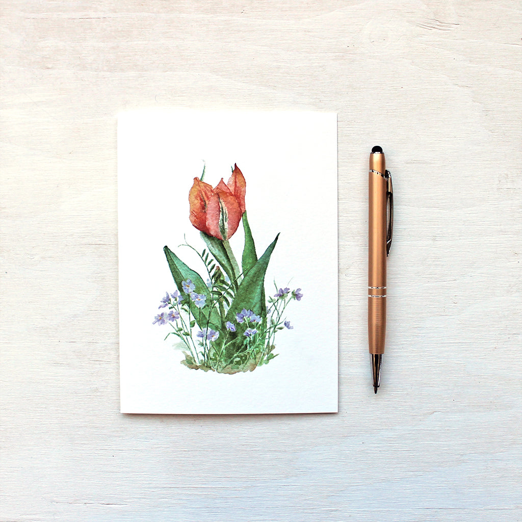 Note card featuring a watercolour painting of an orange and red tulip surrounded by spring violets. Artist Kathleen Maunder.