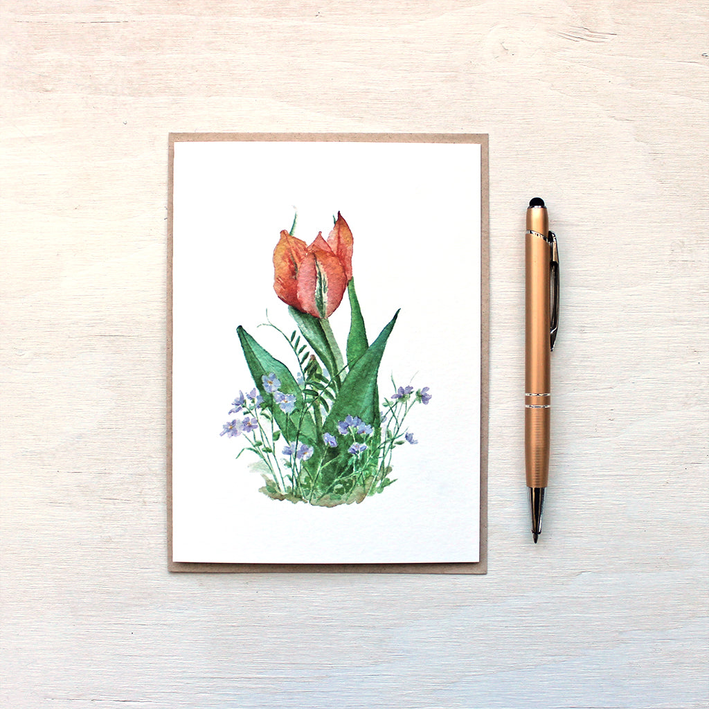 Note card featuring a watercolor painting of an orange-red tulip surrounded by violets. Artist Kathleen Maunder.