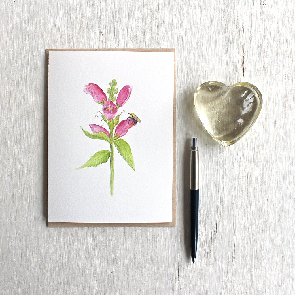 Note card featuring watercolor painting of pink turtlehead flower and a bee. Artist Kathleen Maunder.
