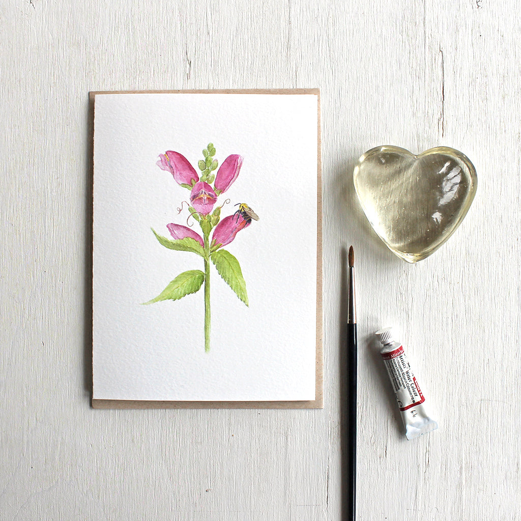 Note card with watercolor painting of pink turtlehead flower and a bee. Artist Kathleen Maunder.