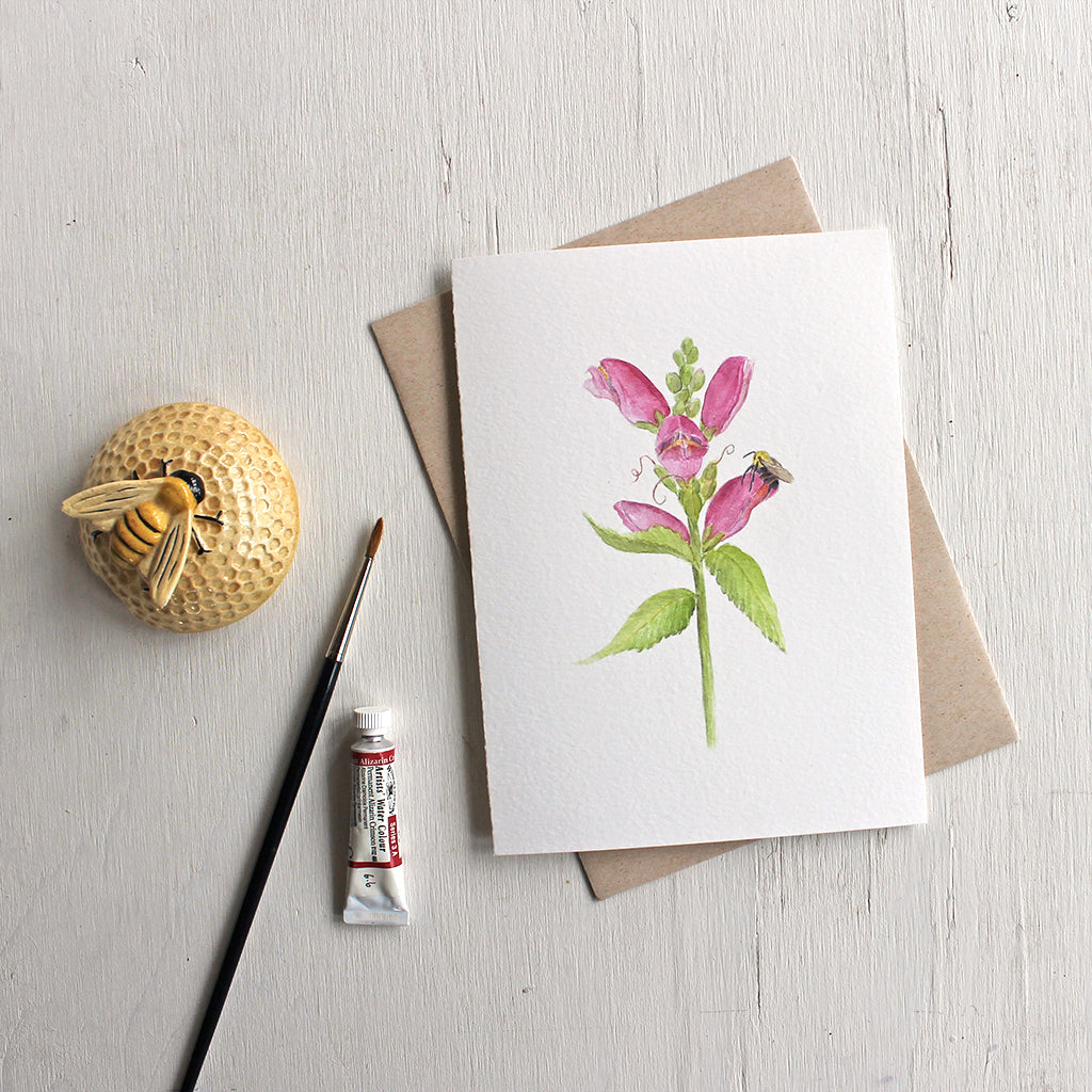Note card featuring watercolor painting of pink turtlehead flower and a bee. Artist Kathleen Maunder.