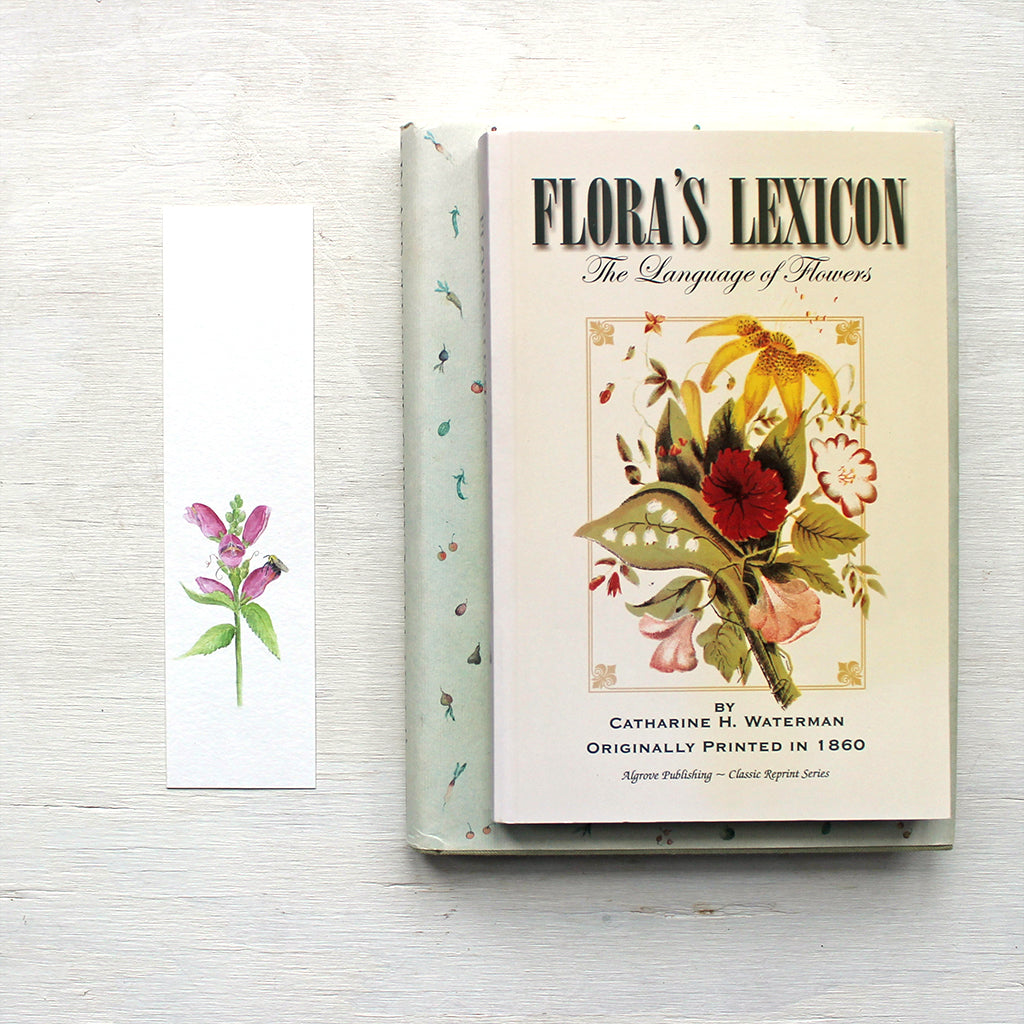 A paper bookmark featuring a watercolor painting of pink turtlehead and a bee. Artist Kathleen Maunder.