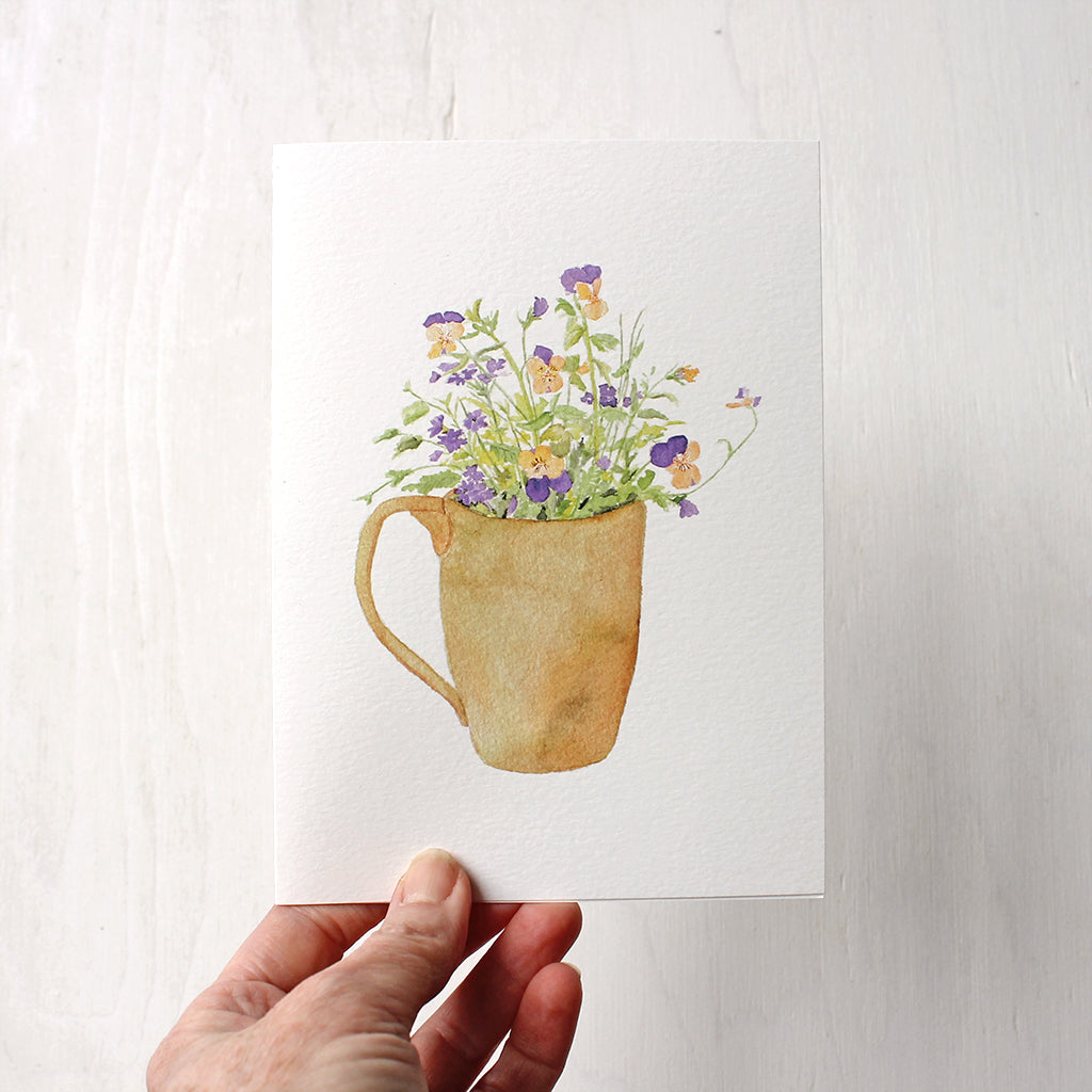A note card featuring a watercolor painting of yellow and purple violas and purple verbena in a ceramic mug. Artist Kathleen Maunder