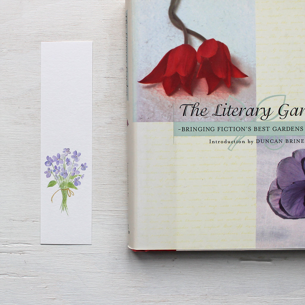 A paper bookmark featuring a watercolour painting of a posy of violets. Artist Kathleen Maunder.