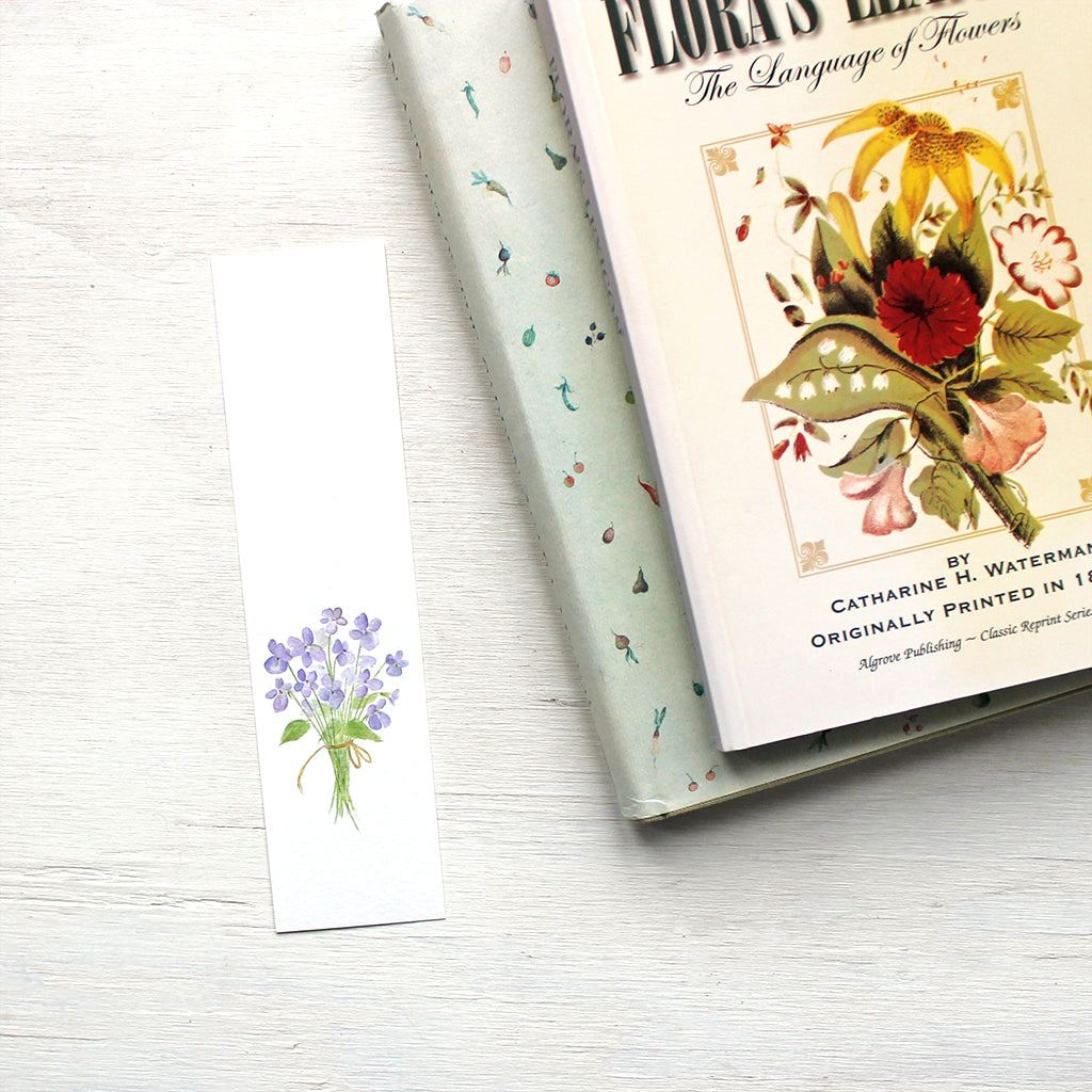 A lovely paper bookmark featuring a delicate watercolor painting of a bouquet of violets. Artist Kathleen Maunder.