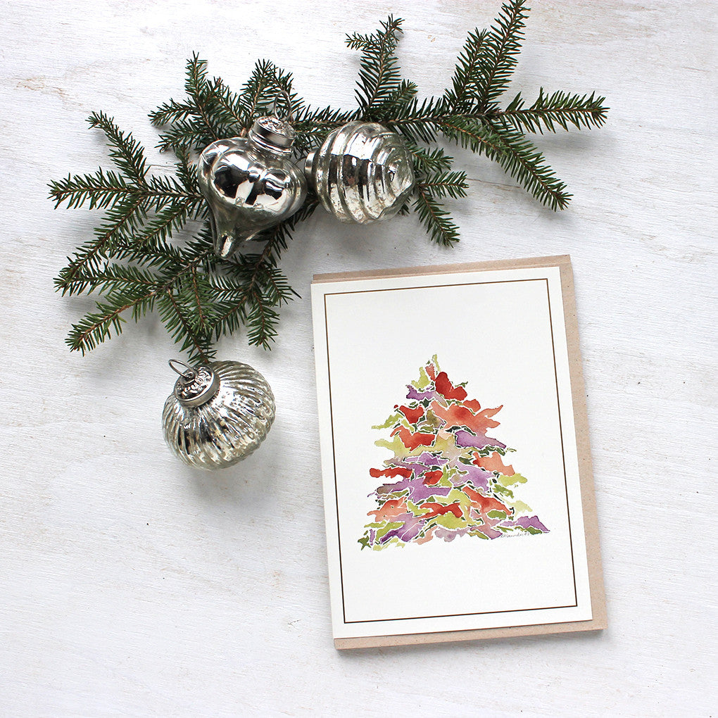 A holiday card featuring a multi-coloured Christmas tree painted in watercolor. Festive tones of red, green and purple. Artist Kathleen Maunder