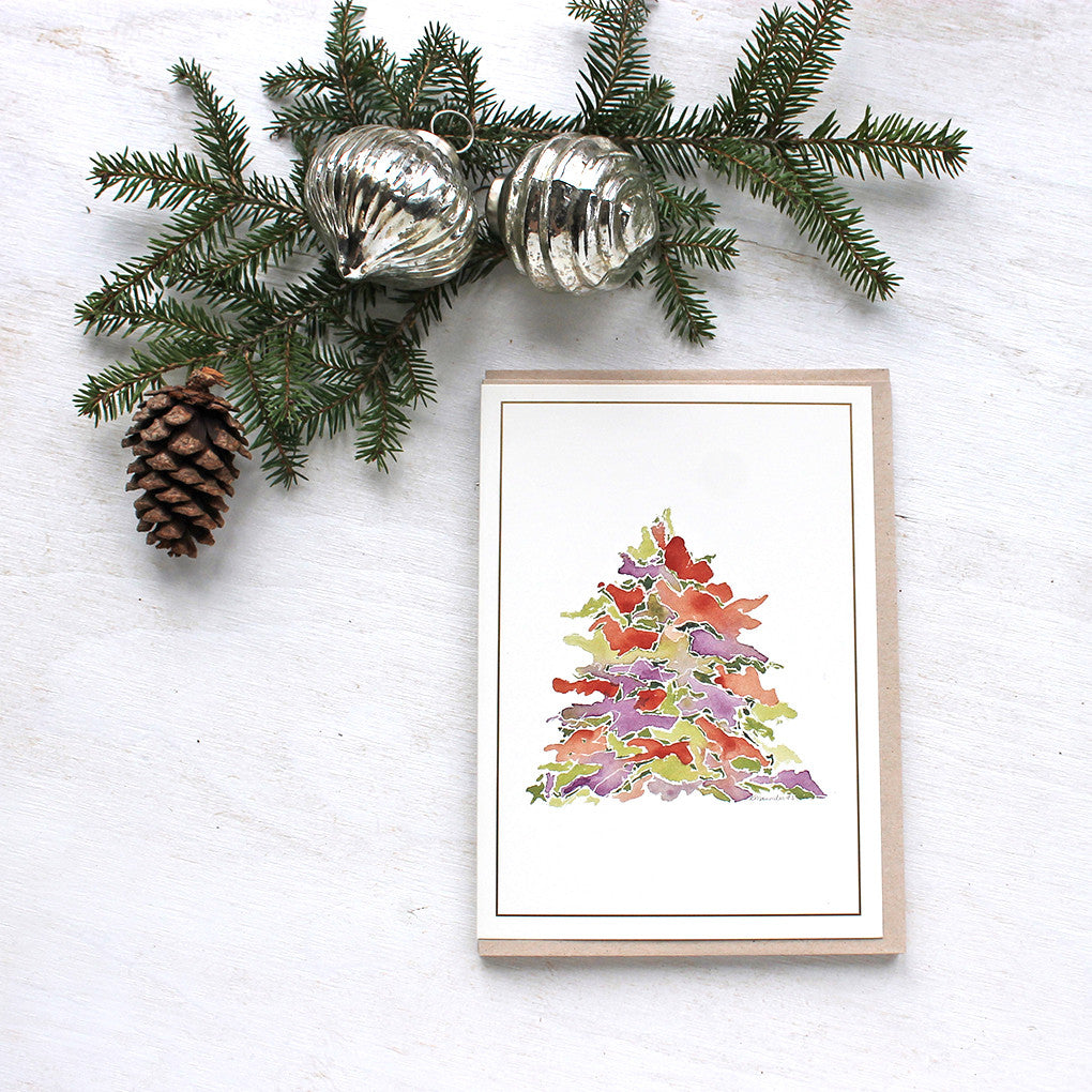 A holiday card featuring a multi-coloured Christmas tree painted in watercolor. Festive tones of red, green and purple. Artist Kathleen Maunder