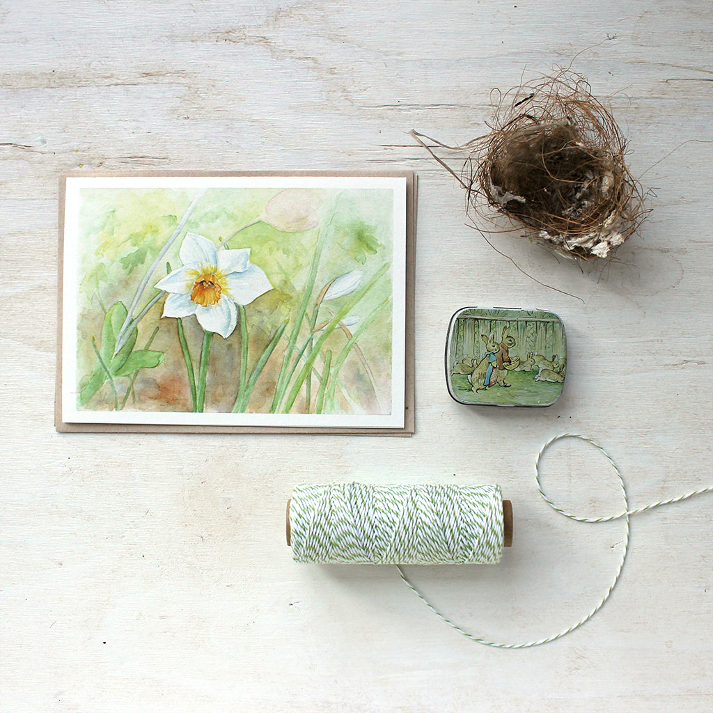 A botanical note card featuring a watercolor painting of a single white and yellow daffodil (narcissus) in a spring garden. Artist Kathleen Maunder.