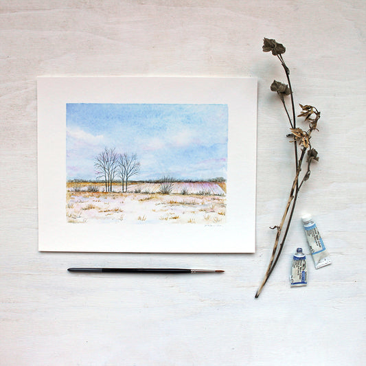 An art print featuring a watercolor painting of a snow covered rural field with a lovely sky filled with soft clouds. Artist Kathleen Maunder.