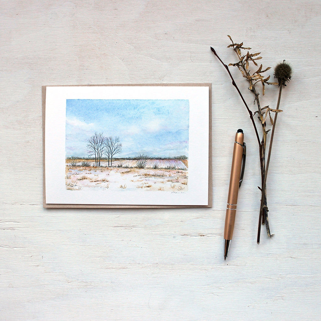 A blank note card featuring a watercolor painting of a snowy rural field and beautiful cloudy sky. Artist Kathleen Maunder.
