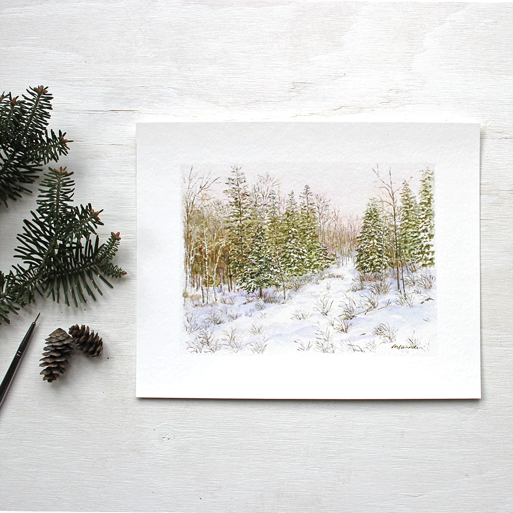 An art print featuring a watercolour of a pathway through a snow covered forest. Artist Kathleen Maunder