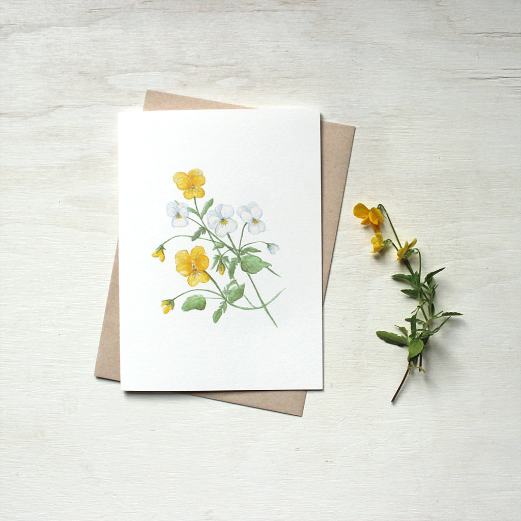 Note card featuring a watercolour painting of yellow and white violas. Accompanied by kraft envelope. Artist Kathleen Maunder.