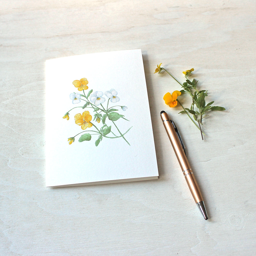 A blank note card featuring a watercolor painting of yellow and white violas.